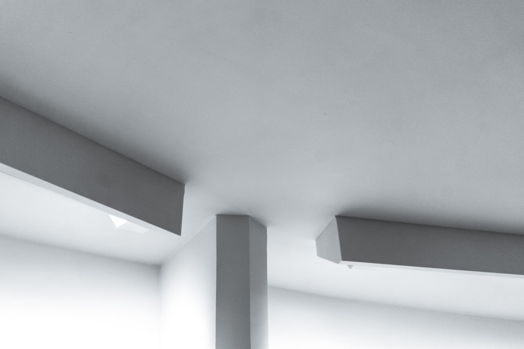 Architectural details in grey and white, where horizontal light fixtures almost meet a narrow vertical column