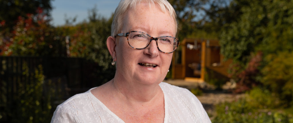 A relaxed portrait in front of a verdant garden and its small wooden summerhouse, which glow in rich greens and oranges in the afternoon sun.